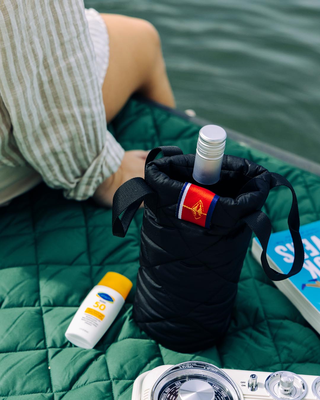 A black puffer wine tote sitting on a green surface with a bottle inside. The tote appears to be made of a quilted design and has a strap for carrying.